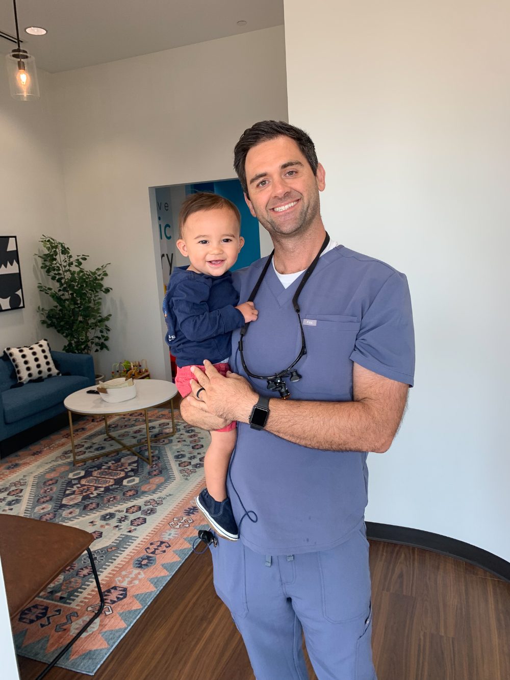 Dr. Matt Scribbins smiling and holding a young patient in the office waiting room